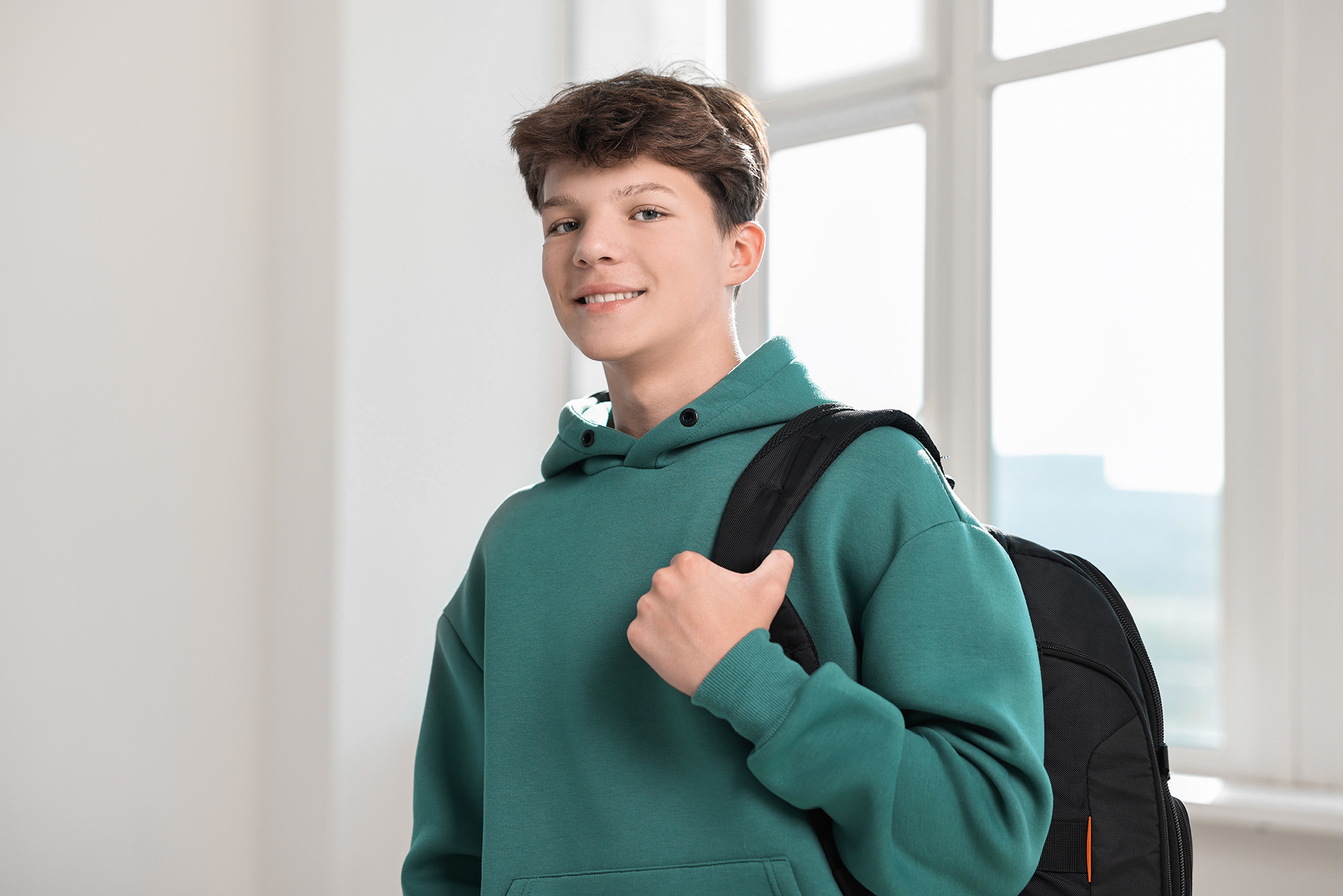 Portrait of happy teenage boy with backpack indoors
