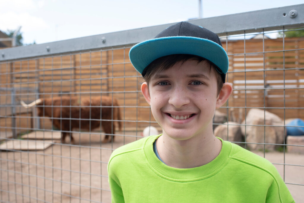 Portrait of a boy at the zoo in front of a fence, with a bull in the background